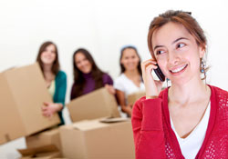 Woman on the phone with women holding moving boxes in the background