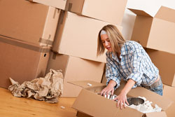Woman packing up a box with a pile of other moving boxes behind her