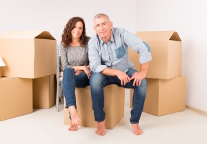 Middle-aged couple sitting on moving box with other boxes surrounding them