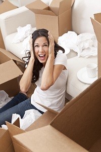 Woman surrounded by moving boxes holding her head in stress
