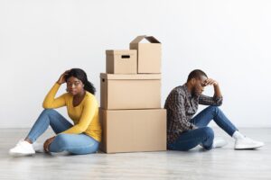 Young couple sitting on the ground with a pile of moving boxes in between them